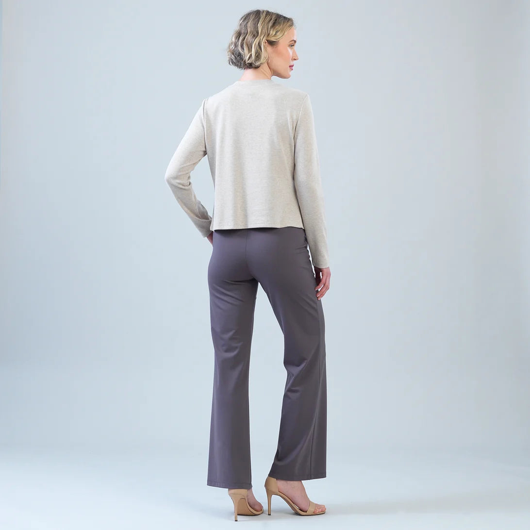 A woman is shown from the back wearing a light beige long-sleeve cropped sweater and dark gray wide-leg trousers, paired with nude high-heeled sandals, against a light gray studio background.