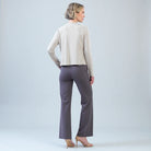 A woman is shown from the back wearing a light beige long-sleeve cropped sweater and dark gray wide-leg trousers, paired with nude high-heeled sandals, against a light gray studio background.