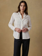 Woman wearing a white shirt and black pants against a beige background
