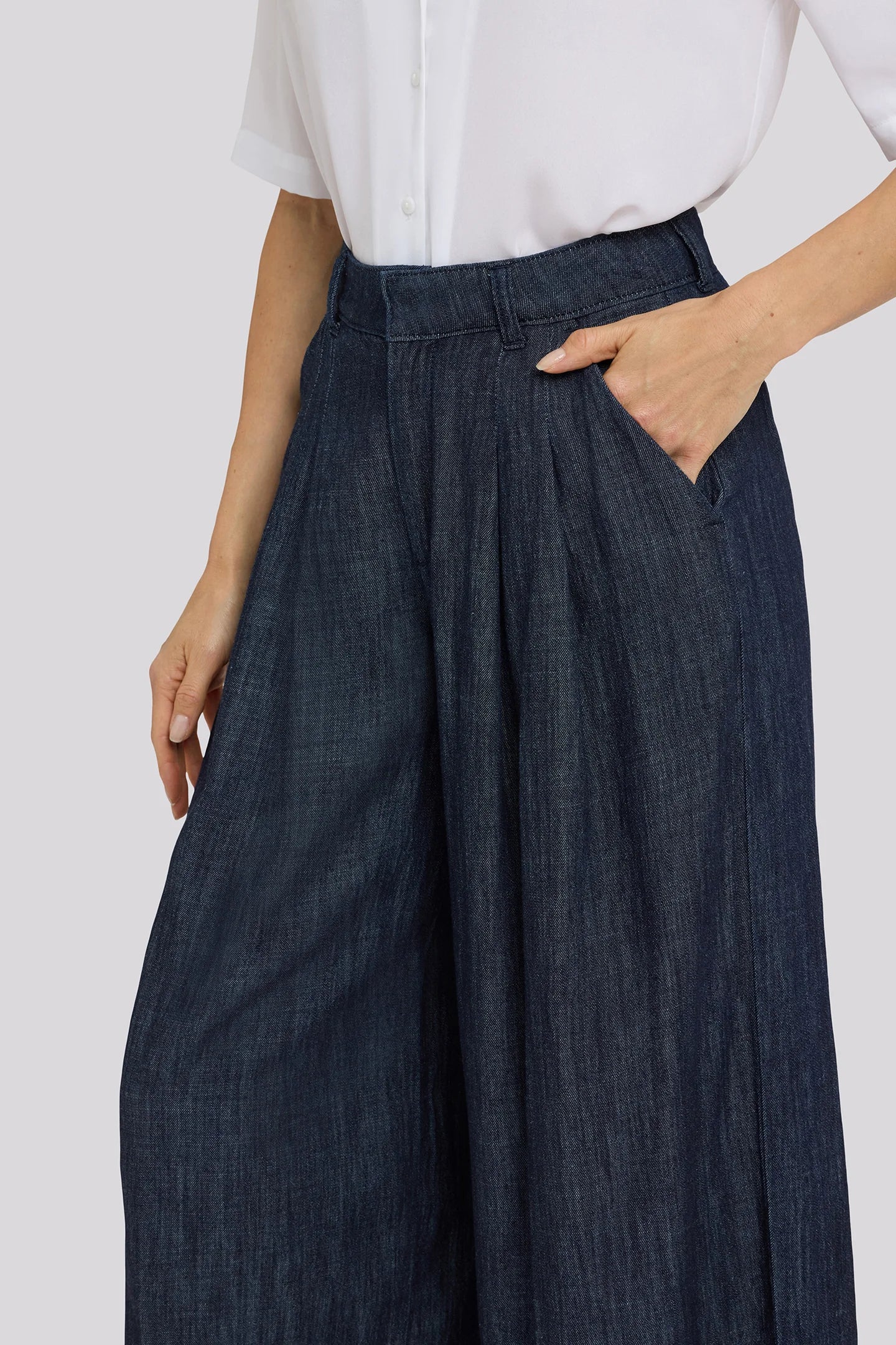 Person wearing dark blue wide-leg pants and a white shirt on a light gray background