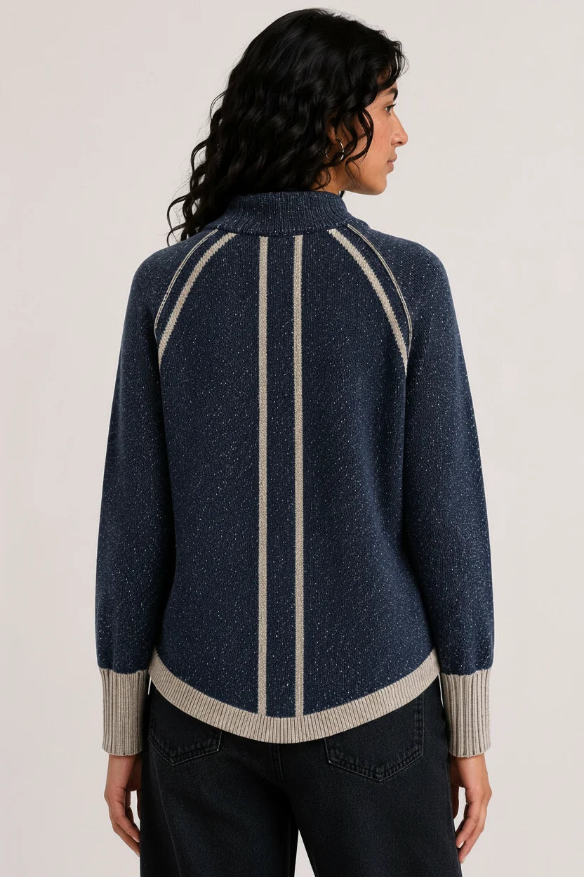 A woman shown from the back wearing a navy blue knit sweater with beige vertical stripes and ribbed trim, paired with dark jeans, against a plain light background.