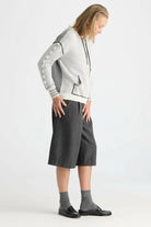 A model wearing a light gray and white knit zip-up hoodie with gray sleeve patches, dark gray knee-length shorts, gray socks, and black loafers, photographed against a plain light gray studio background.