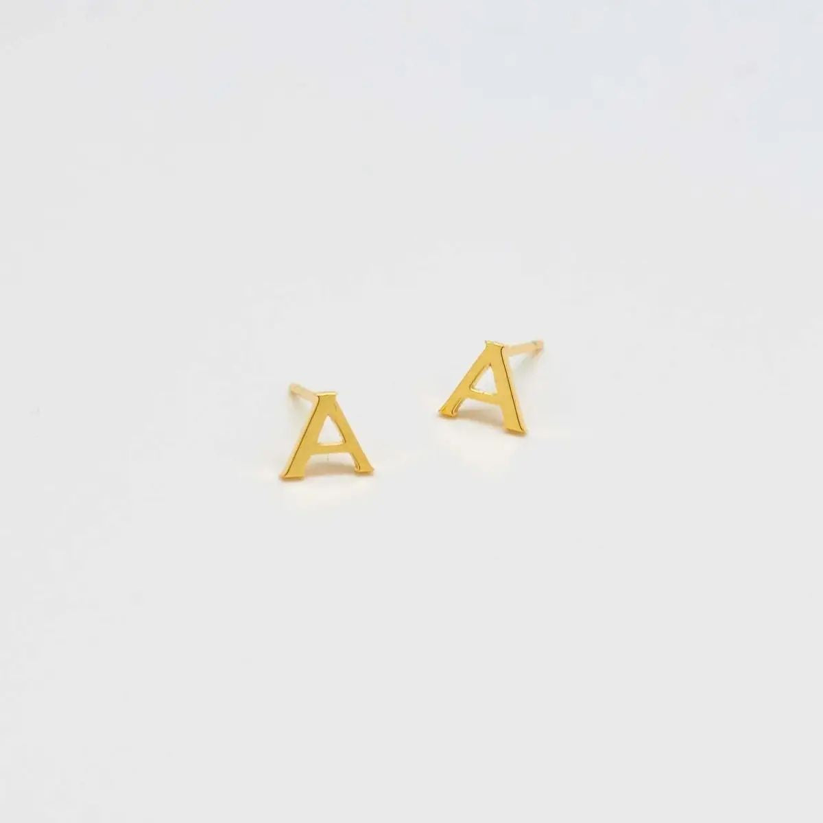 Pair of gold-tone letter A initial stud earrings on a light background