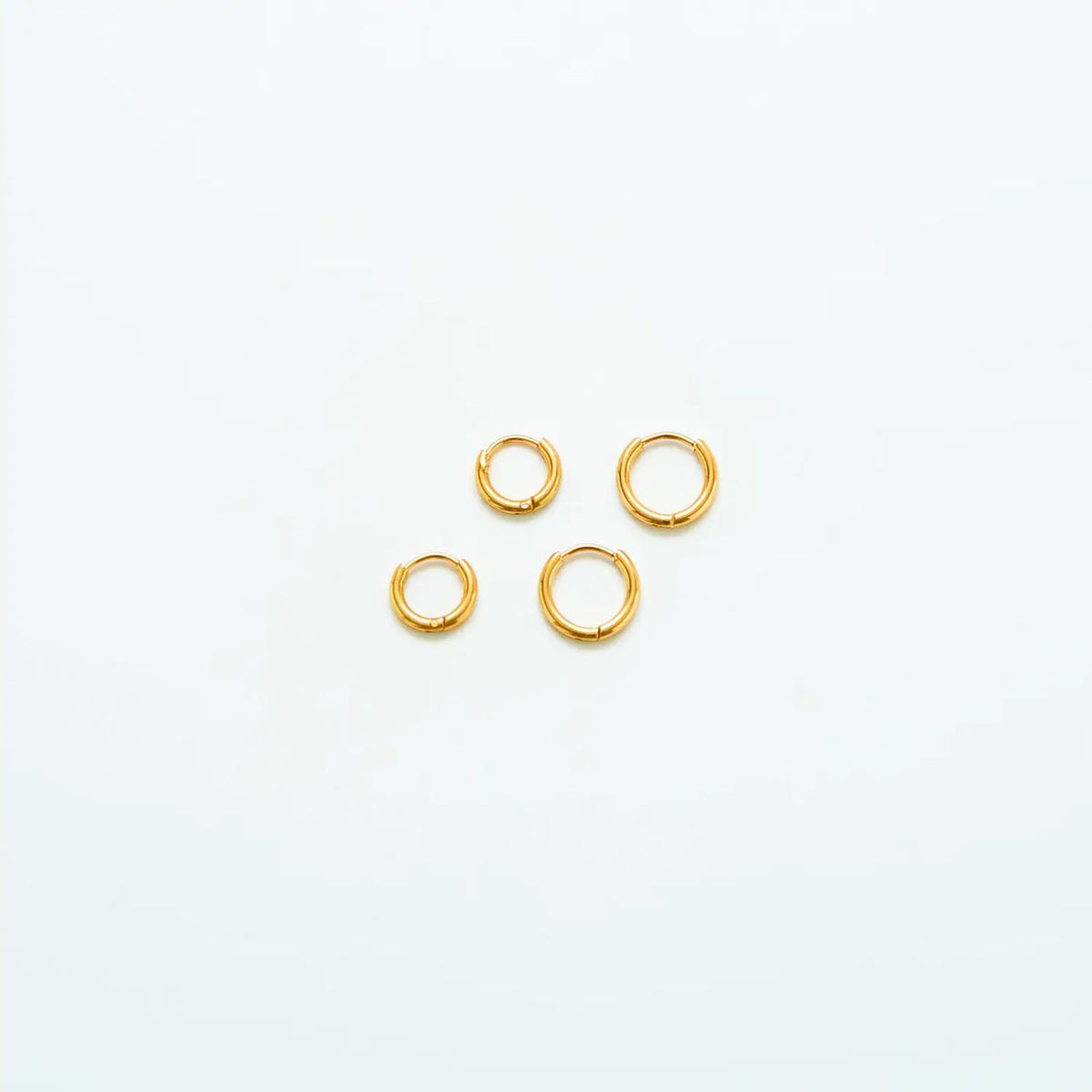 Two pairs of mini gold-tone huggie hoop earrings on a light background