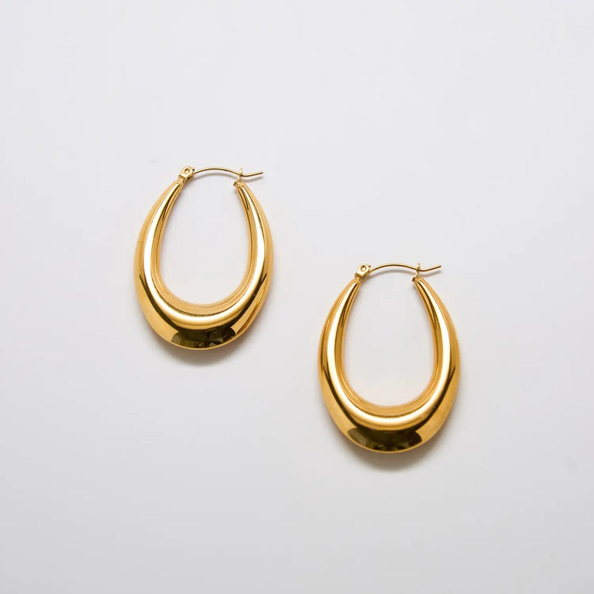 Pair of large gold-tone oval hoop earrings on a light background