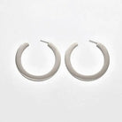 Pair of medium silver-tone flat hoop earrings on a light background