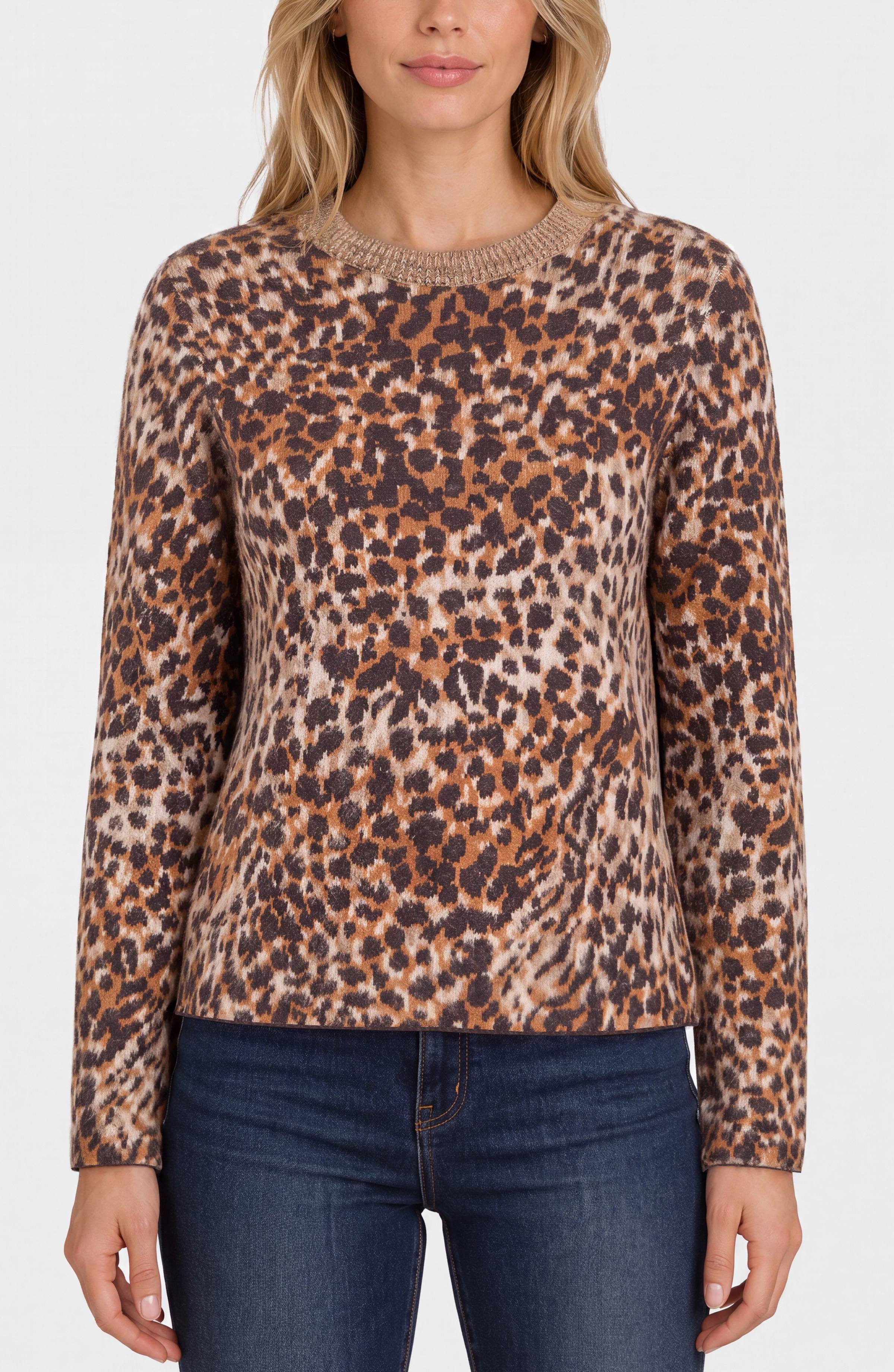 A woman wearing a long-sleeve crewneck sweater with a brown, beige, and black leopard print pattern, paired with dark blue jeans, against a plain light gray background.