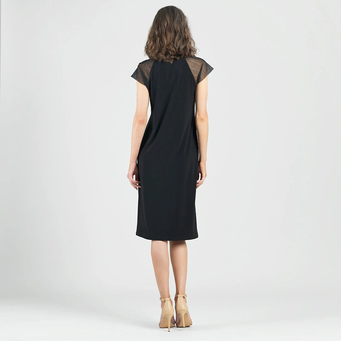 A woman viewed from behind wearing a black knee-length dress with sheer mesh cap sleeves, paired with beige high-heeled sandals, against a light gray studio background.