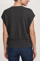 A woman shown from the back wearing a dark charcoal gray knit sweater with short dolman sleeves and a ribbed hem, paired with blue jeans against a light gray studio background.