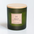 A dark green frosted glass soy candle jar with a light wood lid and a beige paper label reading 'CHALET' and 'GXP CO.', photographed on a clean white background.