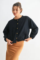Woman wearing a black cardigan with gold buttons on a white background
