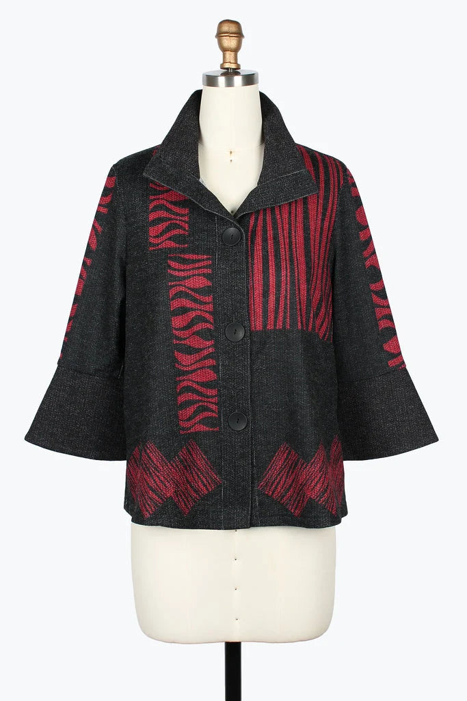 A cropped button-front jacket displayed on a cream dress form. The jacket has a dark charcoal gray base with bold red geometric and zebra-like patterned panels.
