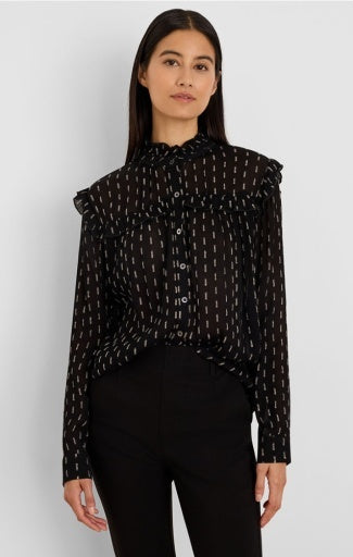 A woman modeling a sheer black long-sleeve blouse with a small white geometric pattern, ruffled shoulders, and a high gathered neckline, paired with black pants against a light gray studio background.