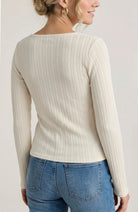 Woman wearing a beige ribbed sweater and blue jeans against a plain background