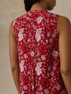 Red sleeveless top with white floral pattern worn by a person against a beige background