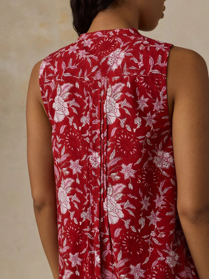 Red sleeveless top with white floral pattern worn by a person against a beige background