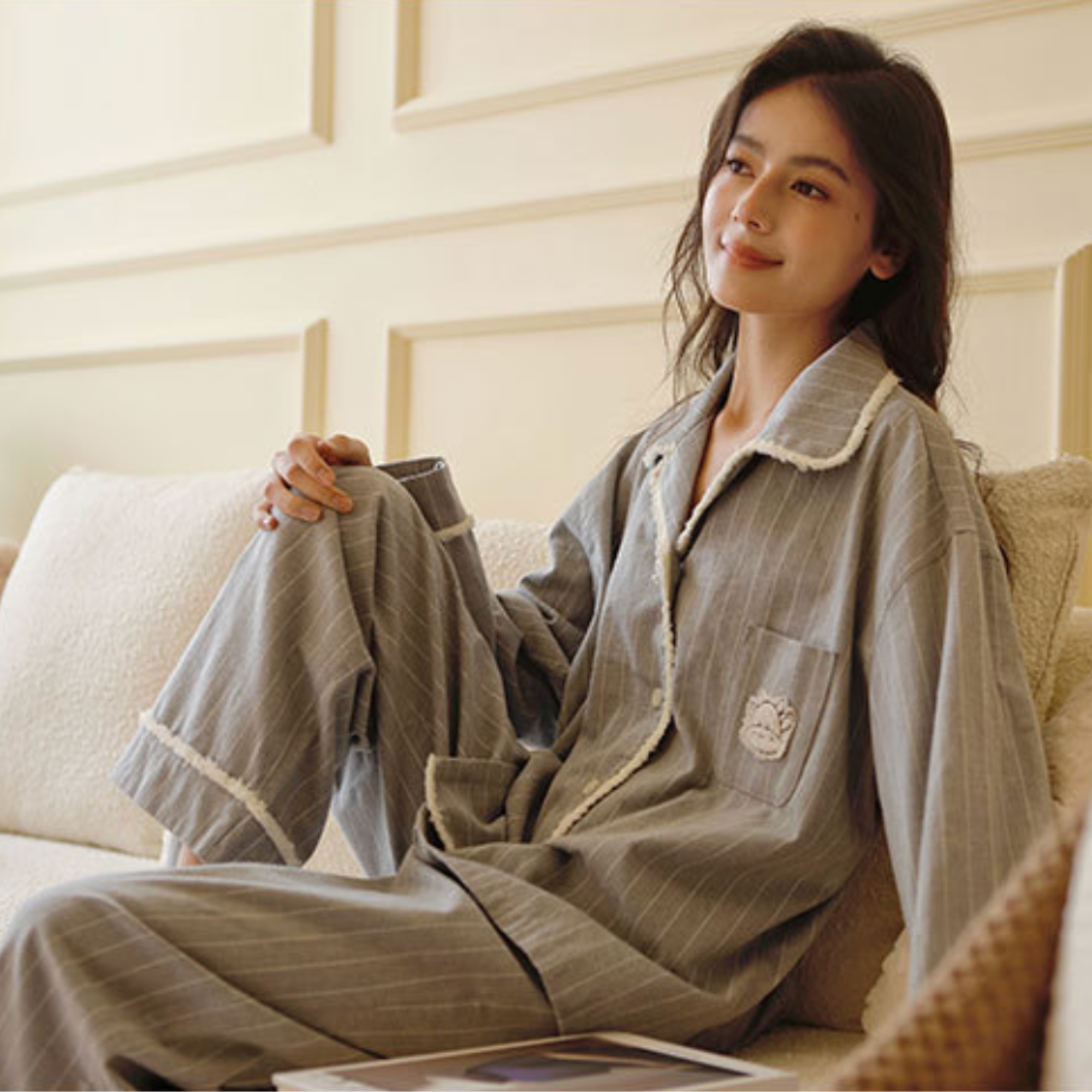 Woman lounging in the grey flannel pajama set on a cream sofa