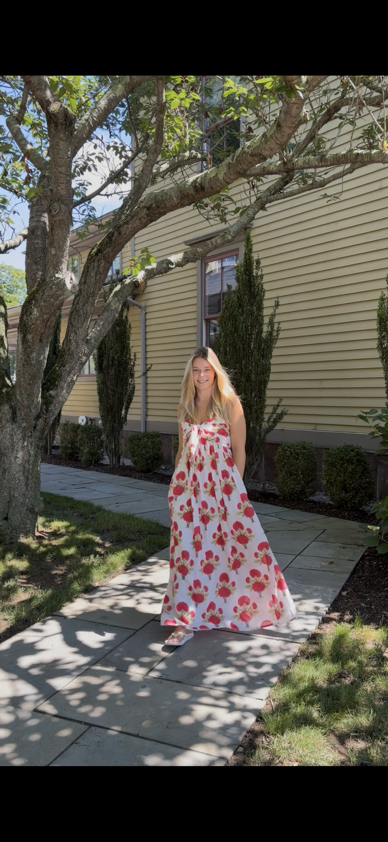 Faherty Voile Alexi Dress in Bloom Poem white with red and green floral print, flowing A-line maxi worn outdoors, front view
