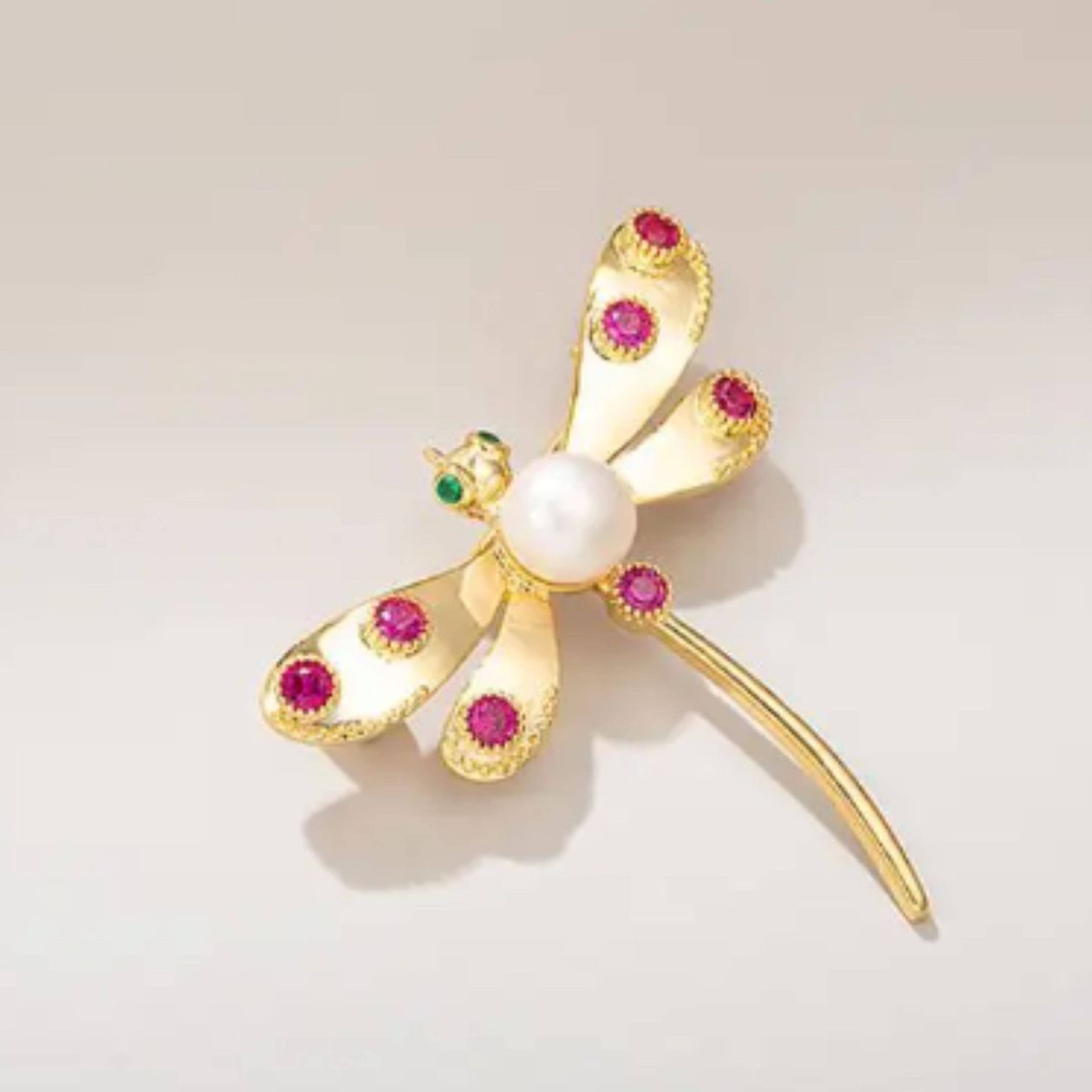 Gold dragonfly brooch with pearls and gemstones on a light background