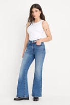 Woman wearing blue flared jeans and a white top on a white background