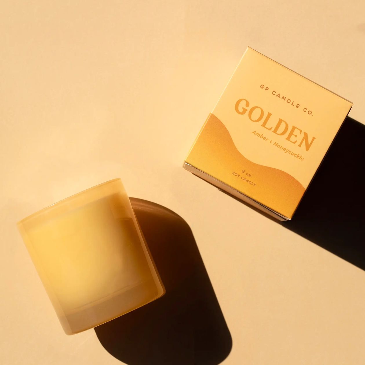 GP Candle Co. Golden Hue candle in a frosted glass jar beside its yellow gift box on a warm beige surface