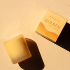 GP Candle Co. Golden Hue candle in a frosted glass jar beside its yellow gift box on a warm beige surface