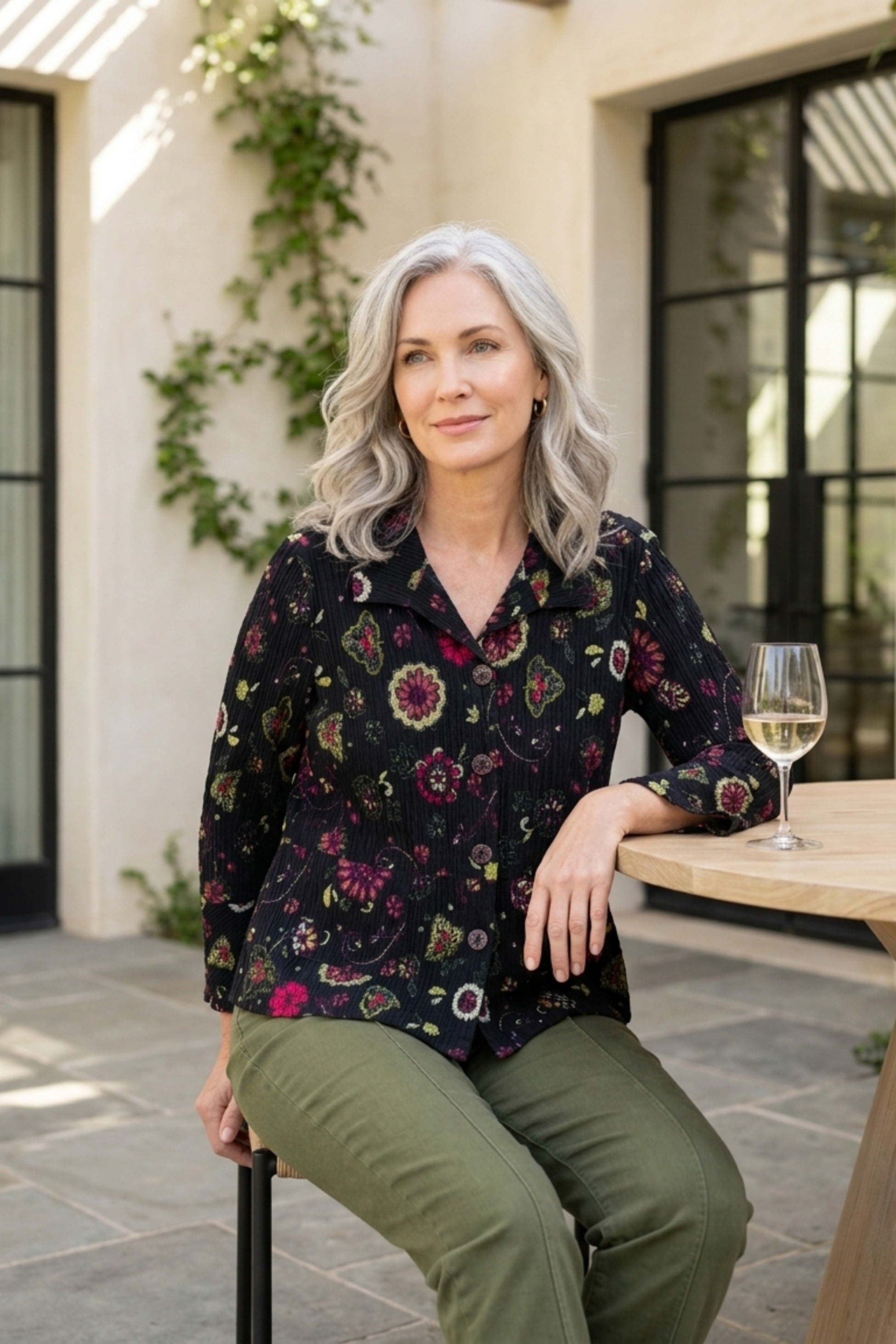 Habitat Crinkle Floral Flounce Jacket in black floral print worn with olive pants, seated on a patio