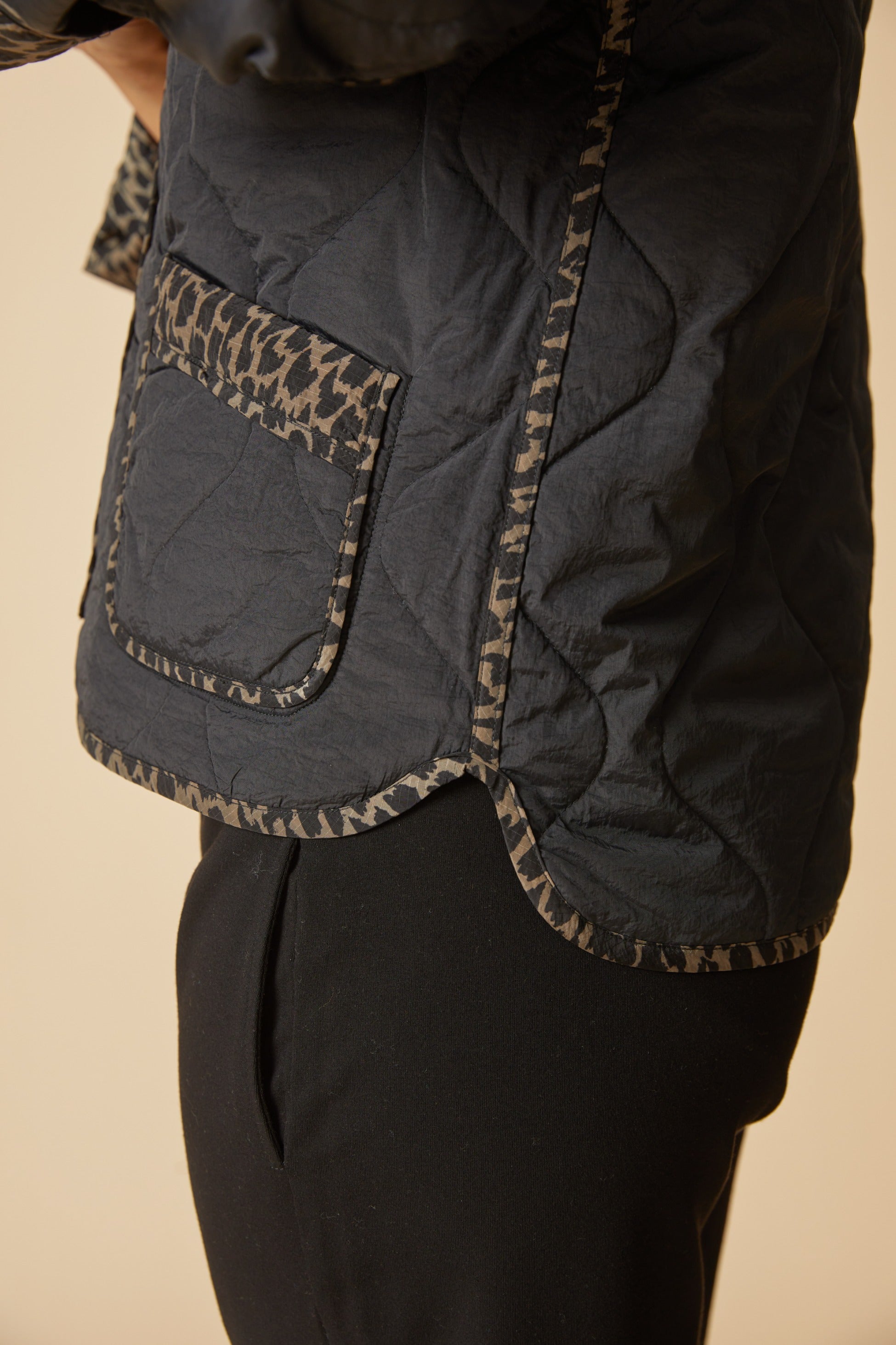 Close-up of the Habitat Reversible Print Quilt Puffer Coat pocket and hem with animal print trim on black quilting