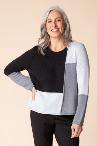 Woman wearing the Habitat Yin Yang Block Party Sweater in Mist, black, grey and pale grey color-block crewneck with black pants