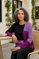 Woman wearing the Habitat Yin Yang Block Party Sweater in Plum, seated at an outdoor cafe