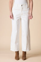 A model from the waist down wearing white cropped wide-leg jeans with tonal embroidery on the lower legs, paired with brown suede ankle boots against a solid beige background.