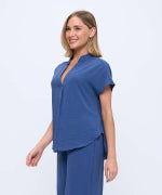 A woman modeling a blue short-sleeve scrub top and matching pants against a plain light gray studio background.