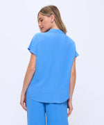 A woman wearing a bright blue short-sleeve scrub top and matching pants, shown from the back against a plain white background.