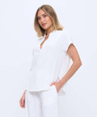 A woman modeling a white short-sleeve top and matching white pants against a plain white studio background.