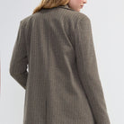 A woman shown from the back wearing a brown textured blazer with blue jeans, photographed against a light gray studio background.