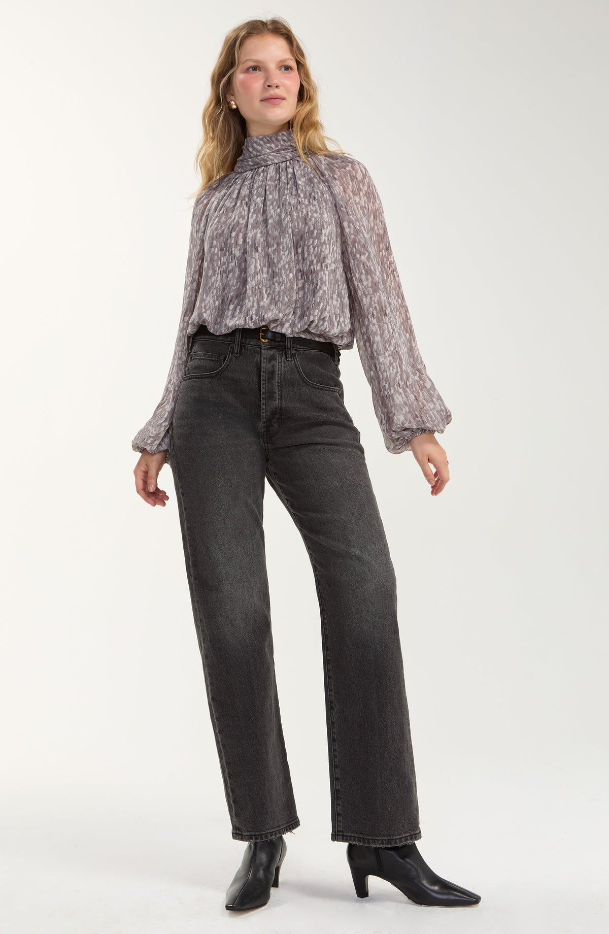 Model wearing the Liverpool grey multi shirred mock neck top tucked into trousers