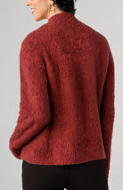 Back view of a woman wearing a rust multi mock-neck pullover sweater in a soft, textured knit, paired with black pants against a light gray studio background.