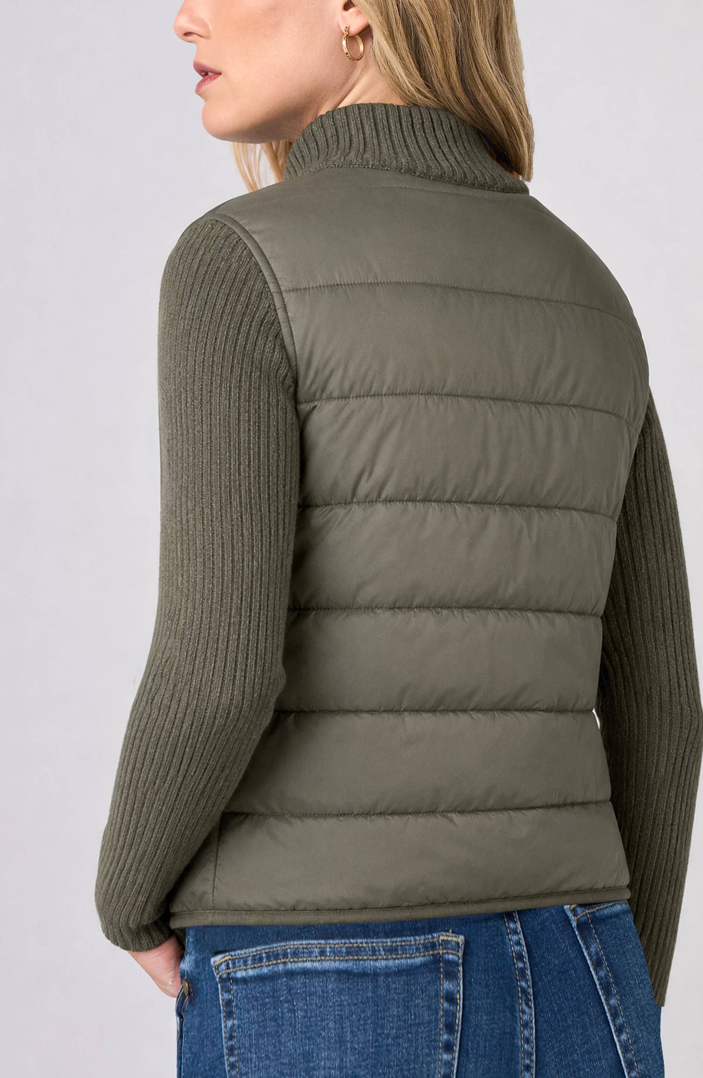 Back view of the Long Sleeve Zip-Front Quilted Sweater Jacket in Heather Olive, showing the quilted puffer back panel and cable-knit sleeves worn with jeans.