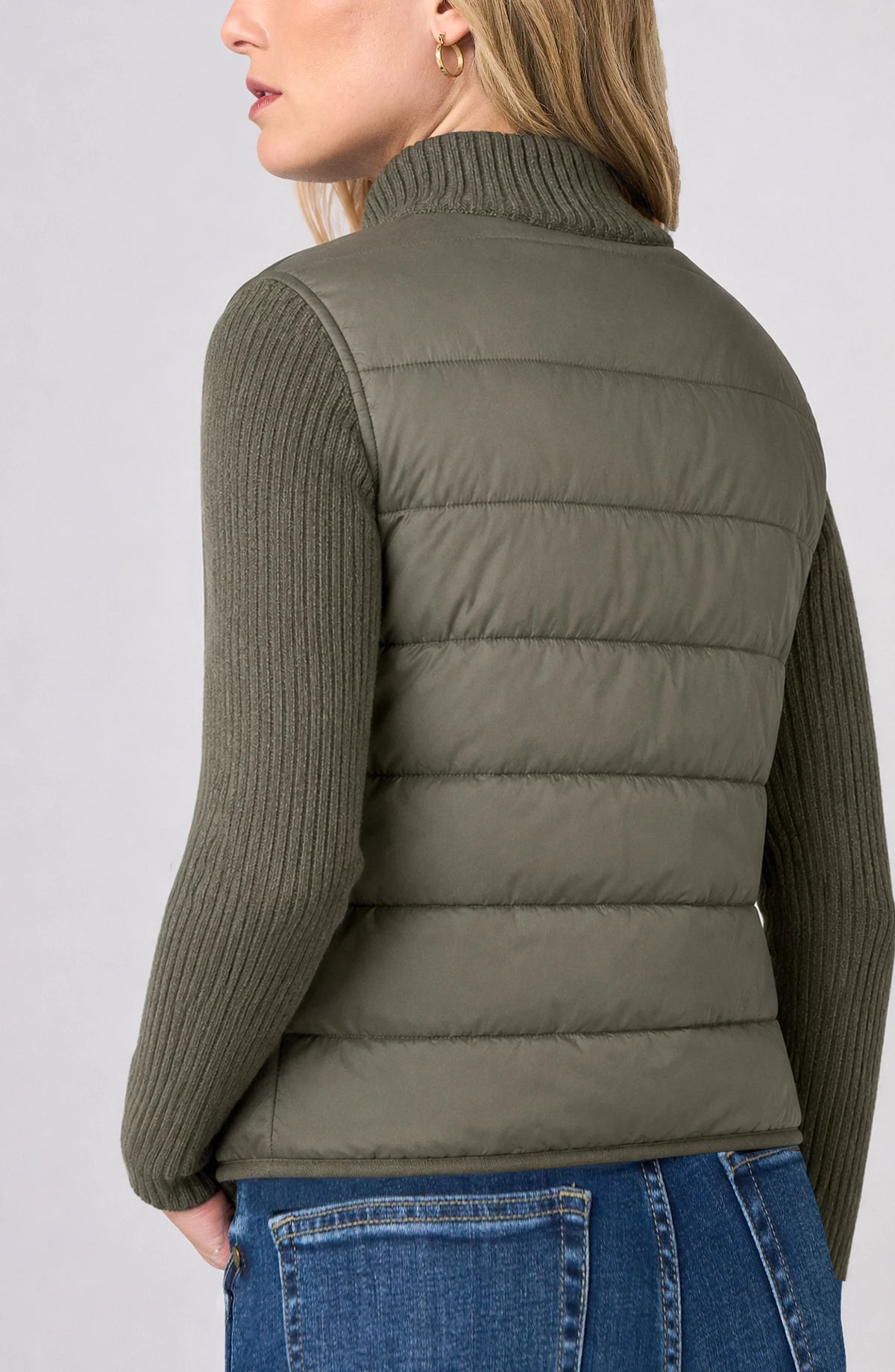 Back view of the Long Sleeve Zip-Front Quilted Sweater Jacket in Heather Olive, showing the quilted puffer back panel and cable-knit sleeves worn with jeans.