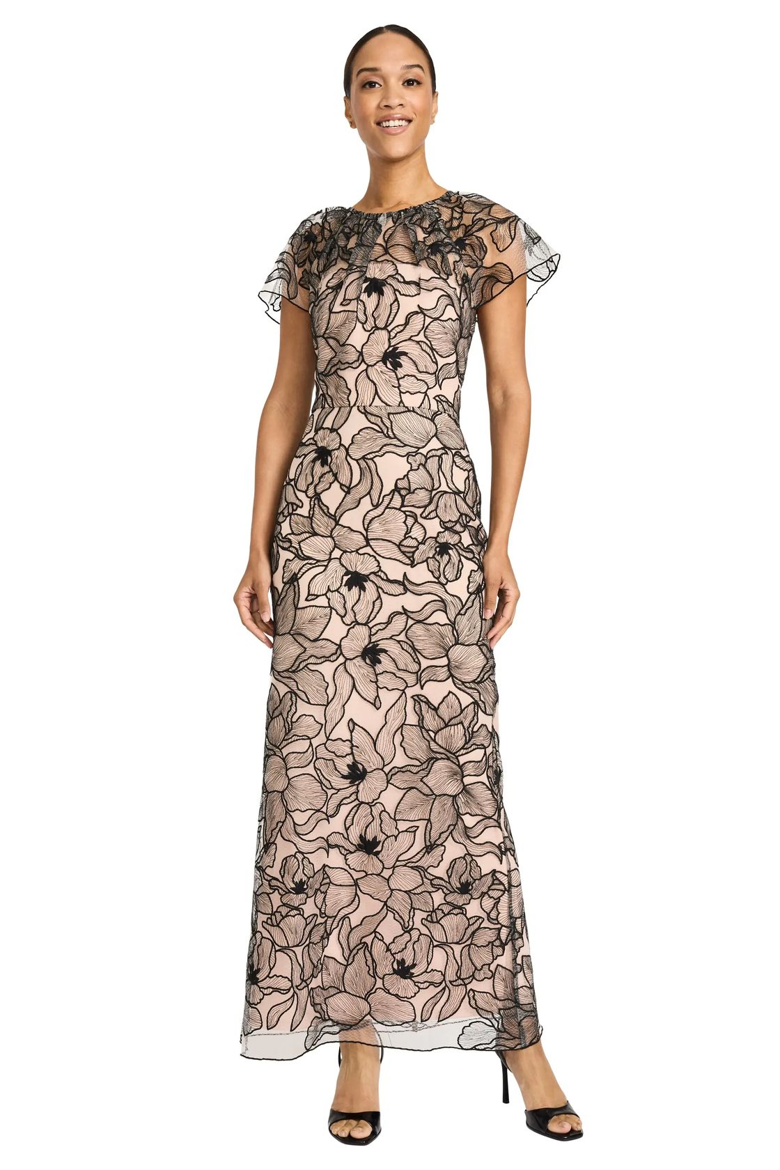 Model wearing the Maggy London Madonna Gown in Black/Blush, a floor-length sheath with black floral embroidery over blush mesh, a sheer illusion neckline and short sleeves