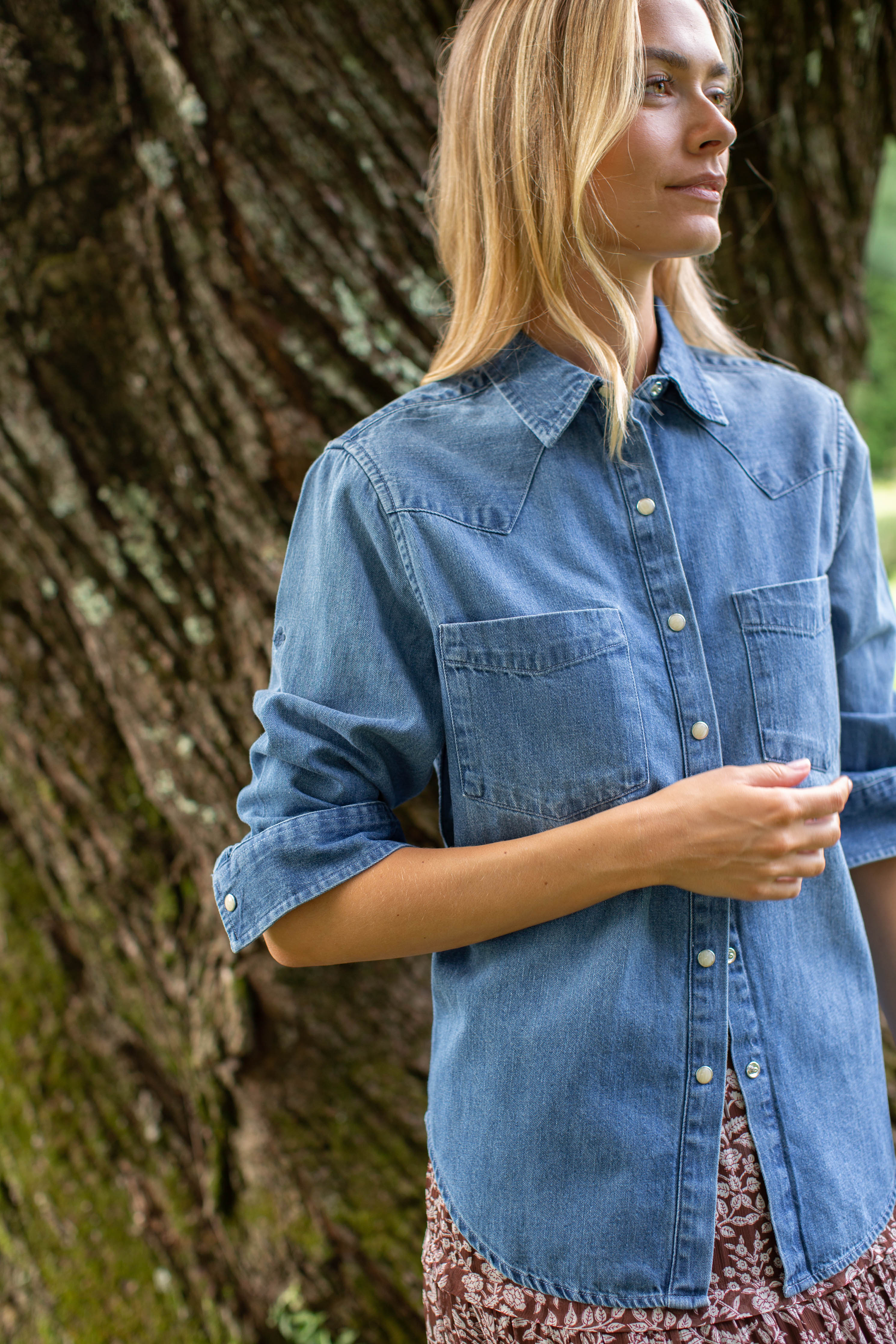 Woman wearing the MAREA western shirt in blue with sleeves rolled, styled with a floral skirt outdoors