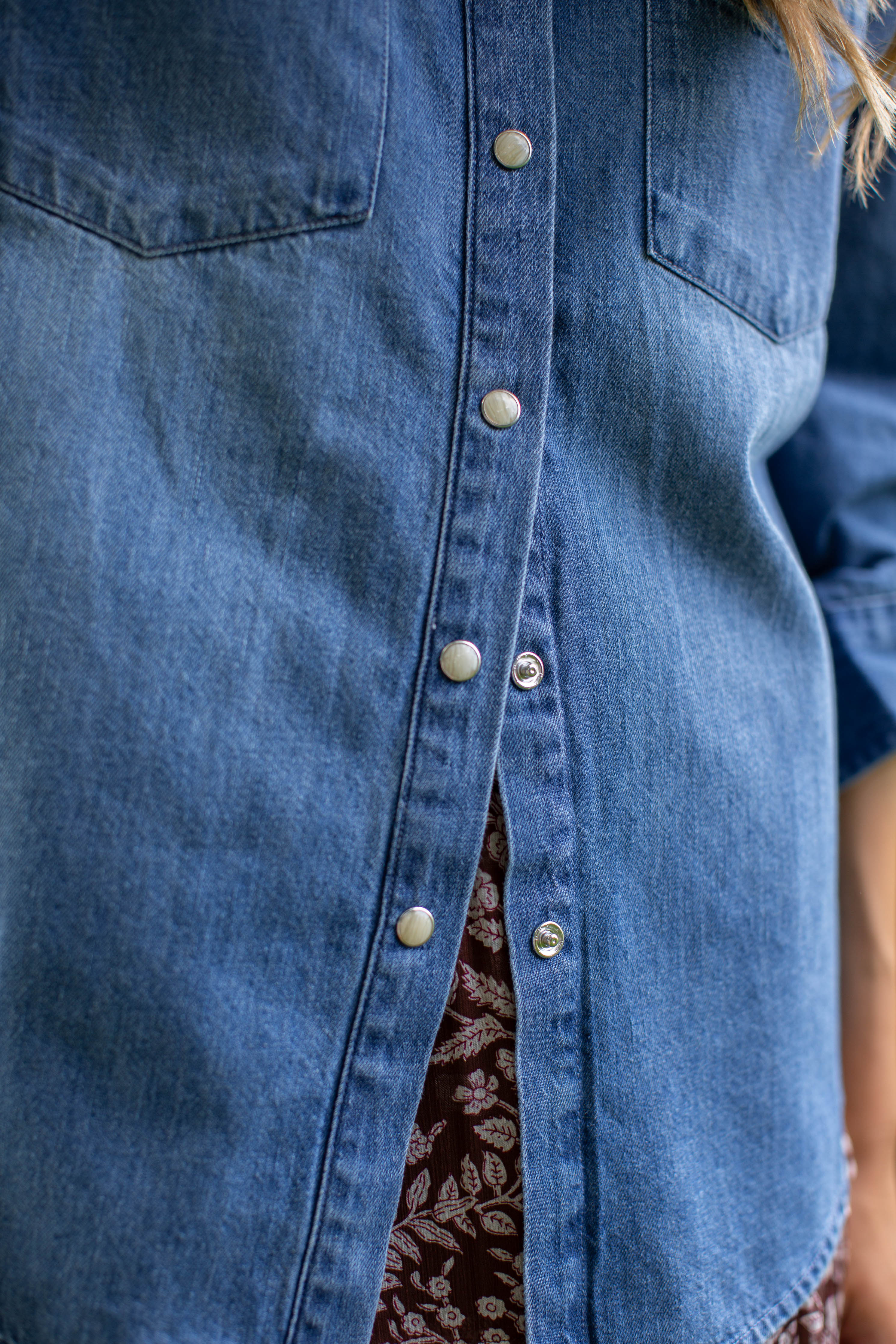 Close-up of the MAREA western shirt in blue showing silver-toned snap buttons and the hem over a patterned skirt