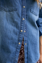 Close-up of the MAREA western shirt in blue showing silver-toned snap buttons and the hem over a patterned skirt