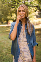 Woman in a park wearing the MAREA western shirt in blue worn open as a layer over a patterned dress