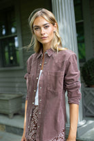 Woman standing on a porch in the MAREA western shirt in brown corduroy, worn open over a white tee and patterned skirt