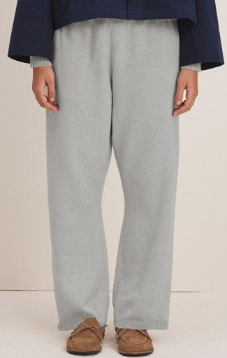 A person wearing light gray knit wide-leg pants with a navy blue top and brown slip-on shoes, shown from the chest down against a plain light beige studio background.