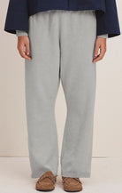 A person wearing light gray knit wide-leg pants with a navy blue top and brown slip-on shoes, shown from the chest down against a plain light beige studio background.