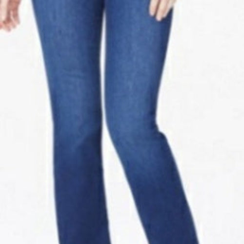 A woman modeling NYDJ Barbara Bootcut petite jeans in Quinn medium blue wash, paired with a white top and beige heeled sandals, against a plain light studio background.