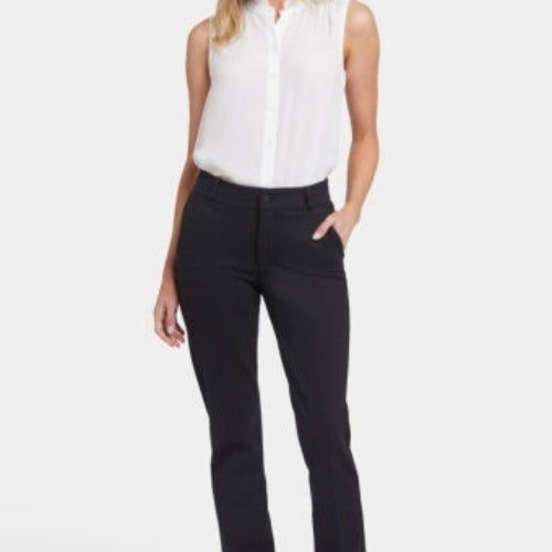 A woman modeling NYDJ Classic Trouser straight-leg pants in black, paired with a white blouse and black flats, against a plain light studio background.
