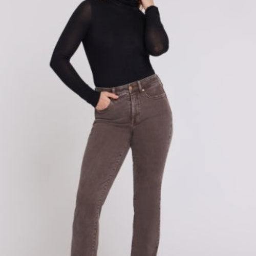 A woman modeling NYDJ High Rise Marilyn Straight petite jeans in Retro Espresso brown wash, paired with a black long-sleeve top and black heeled boots, against a plain light studio background.